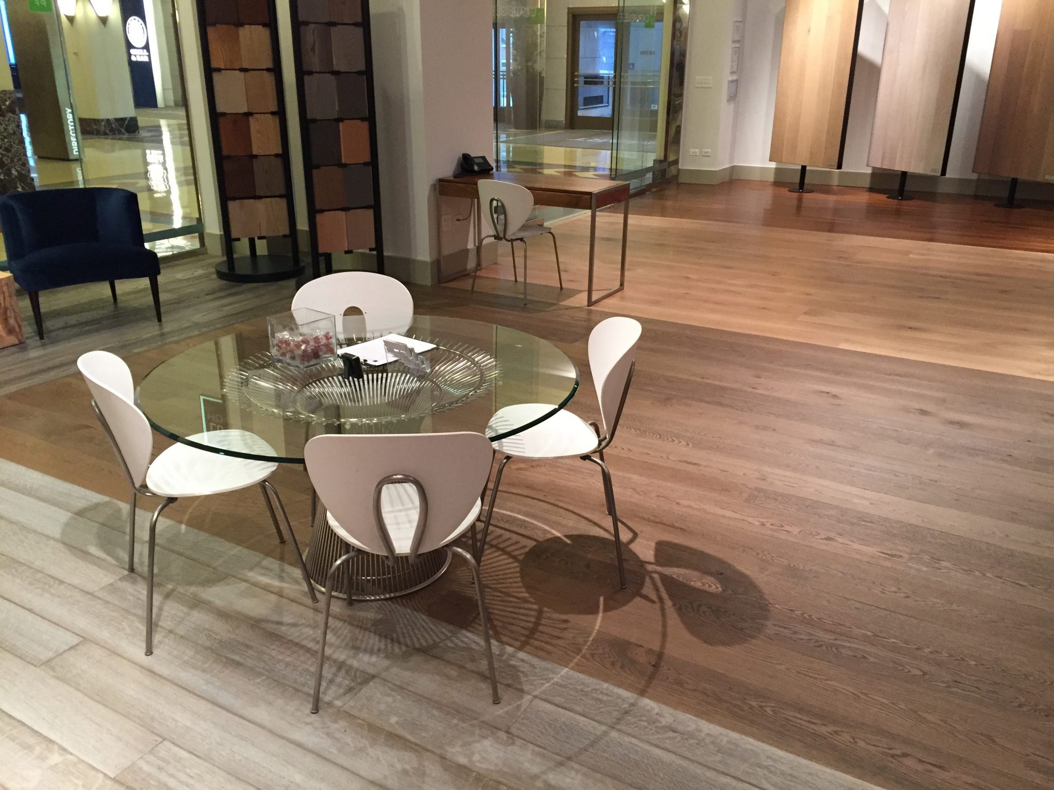 Glass table with white chairs in a modern showroom with wide plank flooring.