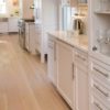 White kitchen with marble island, showcasing modern decor and wide plank flooring.