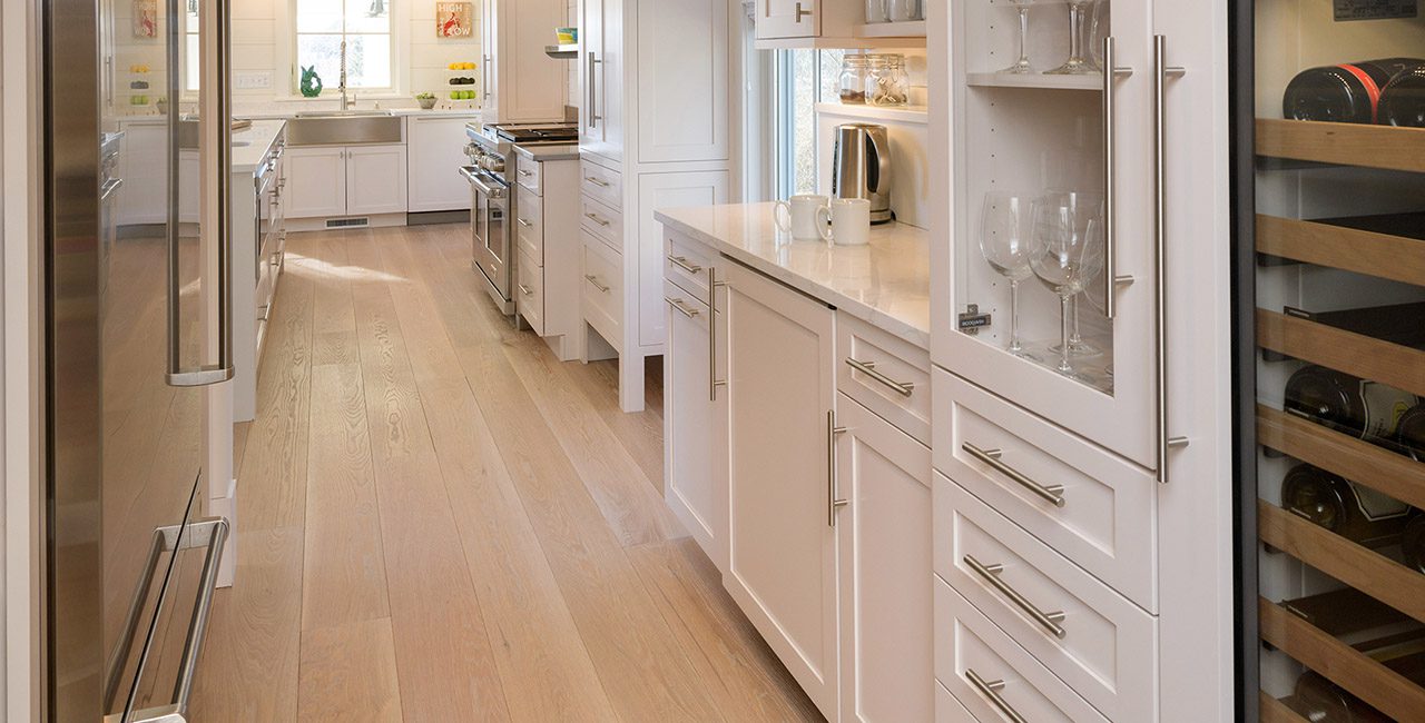 White kitchen with marble island, showcasing modern decor and wide plank flooring.