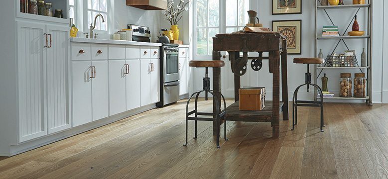 Rustic kitchen with white cabinets, wooden island, and wide plank flooring lit by natural light.