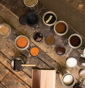 Open wood stain cans and a brush on a table, showcasing stain colors for wood applications.