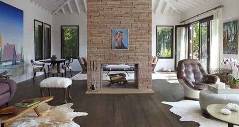 Modern living room with fireplace, windows, wide plank wooden floors, and minimal furniture