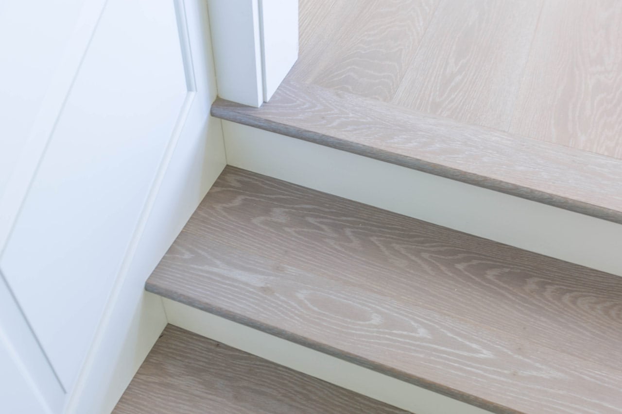 Wooden stairs in light-colored modern interior with wide plank flooring.