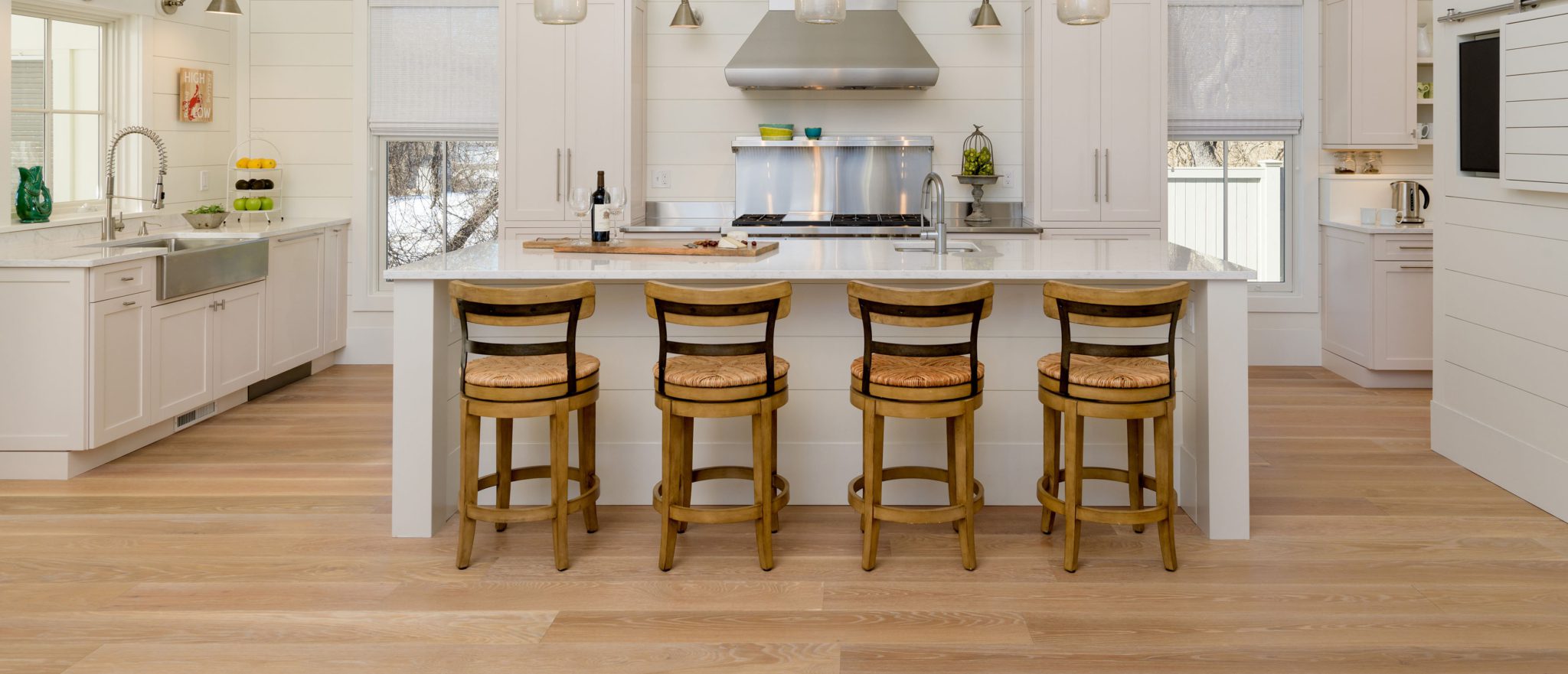 Wooden bar stools at kitchen island with wide plank flooring.