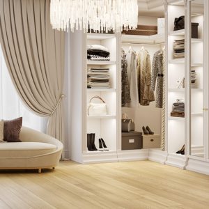 Luxurious walk-in closet with beige sofa, chandelier, and wide plank wooden flooring.