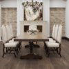 Wooden dining table on wide plank floor, surrounded by ornate chairs.