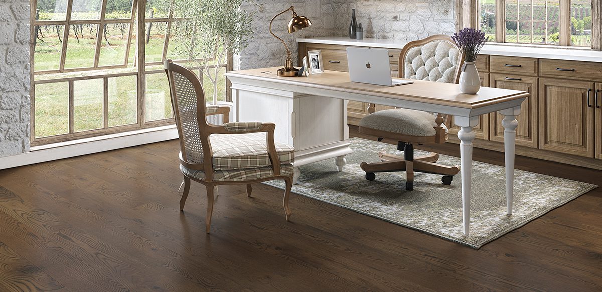 Wooden desk with laptop in an office with wide plank flooring.